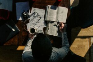 Un jeune homme vu de haut étudiant la Bible et la théologie sur son bureau - Photo de Jacob Bentzinger sur https://unsplash.com/fr/photos/homme-en-chemise-a-manches-longues-noire-ecrivant-sur-papier-blanc-QiLPQeQSXD0
