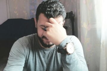 Un homme assis à son bureau, concentré sur ses pensées, et souriant - Photo de Muhmed Alaa El-Bank sur https://unsplash.com/fr/photos/une-personne-avec-la-main-sur-le-visage-tm3MZSG1gEg