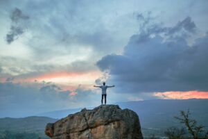 Un jeune homme debout sur un rocher écarte les bras de joie en voyant un coucher de soleil - Photo de Joshua Earle sur https://unsplash.com/fr/photos/man-standing-on-top-of-rock-mountain-during-golden-hour-9idqIGrLuTE