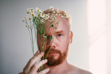 Un homme se cache à moitié derrière quelques fleurs - Photo de Dimmis Vartsur https://unsplash.com/fr/photos/homme-tenant-un-bouquet-de-fleurs-blanches-et-vertes-6va-G7pWa3I