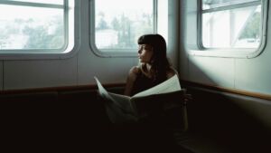 jeune femme lit le journal et regarde par la fenêtre d'un train avec soucis - Photo de Furkan Elverensur https://unsplash.com/fr/photos/une-femme-assise-sur-un-bateau-lisant-un-journal-pmKhCL9UUd0