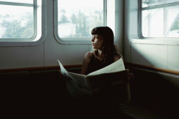 jeune femme lit le journal et regarde par la fenêtre d