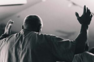 Un homme en chemise simple vu de dos donnant un geste de bénédiction - Photo de Matthew Pablicosur https://unsplash.com/fr/photos/homme-aux-bras-leves-en-signe-dadoration-xk8K_vInhAU