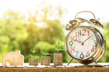 Une composition montrant des piles de pièces qui germent dans de petites pousses et un réveil évoquant le temps qui passe - Image by Nattanan Kanchanaprat from https://pixabay.com/photos/money-finance-mortgage-loan-2696229/