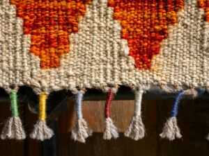 Pièce de tissage avec sa bordure constituée de fils noués colorés - Photo de engin akyurt sur https://unsplash.com/fr/photos/gros-plan-dun-textile-tisse-avec-des-glands-colores-YfYWwgYXGtU