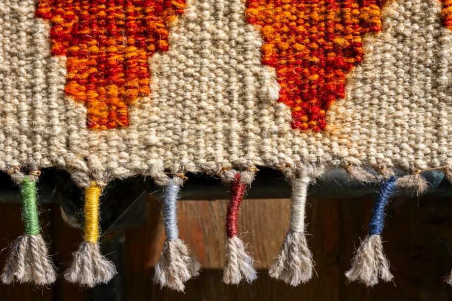 Pièce de tissage avec sa bordure constituée de fils noués colorés - Photo de engin akyurt sur https://unsplash.com/fr/photos/gros-plan-dun-textile-tisse-avec-des-glands-colores-YfYWwgYXGtU
