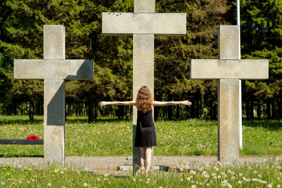 Fillette se tenant les bras en croix devant un calvaire avec trois grandes croix en pierre - Photo de Margo Evardson sur https://unsplash.com/fr/photos/une-fille-debout-entre-trois-grandes-croix-de-pierre-a-lexterieur-F-DHl2JU7lI