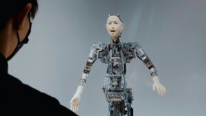un homme portant un masque fait face à un robot au visage humanoïde - Photo de Taiki Ishikawa sur https://unsplash.com/fr/photos/une-femme-regardant-un-robot-dans-les-airs-PXVuoedN8fI