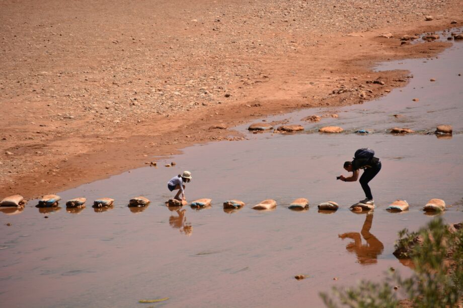 Une fillette essaye de traverser une rivière en marchant sur des pierres, son père la photographie - Photo de Dani Zapater sur https://unsplash.com/fr/photos/quelques-personnes-qui-se-tiennent-dans-leau-38ePPQLXmLg
