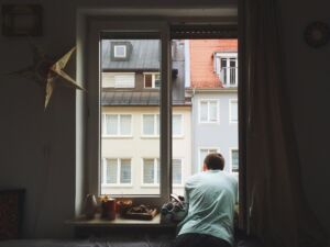 Un jeune homme à la fenêtre de son petit appartement encombré - Photo de Ellen Tanner sur https://unsplash.com/fr/photos/homme-pres-de-la-fenetre-AHLC9O0bxVo