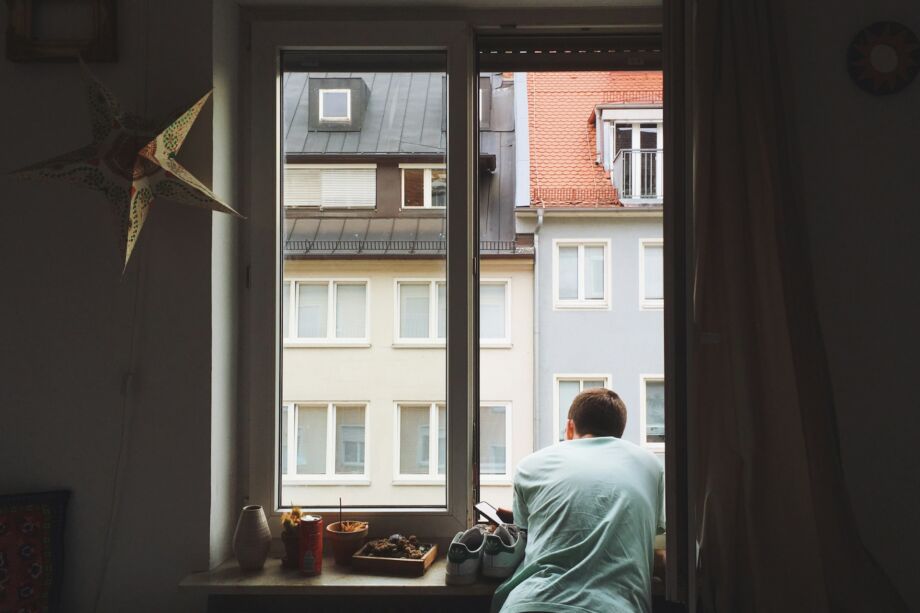 Un jeune homme à la fenêtre de son petit appartement encombré - Photo de Ellen Tanner sur https://unsplash.com/fr/photos/homme-pres-de-la-fenetre-AHLC9O0bxVo