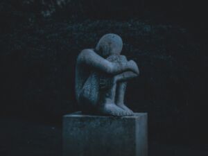 Une statue représentant un homme recroquevillé dans la pénombre d'un parc - Photo de K. Mitch Hodge sur https://unsplash.com/fr/photos/homme-etreignant-sa-statue-de-genou-IqSaG9zv2e0